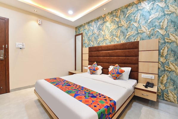 Una habitación de hotel con una cama, una mesita de noche, una pared con diseño de hojas y una puerta.