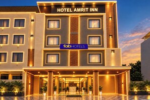 Un hôtel moderne, avec une entrée imposante, de nombreuses fenêtres et une enseigne indiquant qu’il s’agit de l’HÔTEL AMRIT INN.