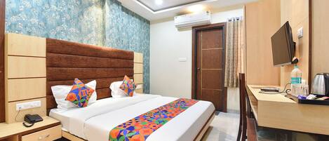 A hotel room with a bed, bedside table, desk, and a television.