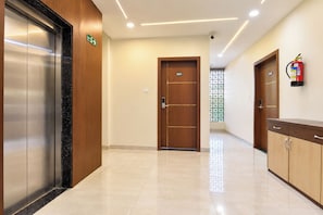 Pasillo de hotel con un ascensor de madera, una puerta con la etiqueta '201' y un extintor en la pared.