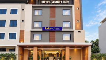 Un hotel de varios pisos con fachada moderna, un llamativo letrero que dice 'HOTEL AMRIT INN' y el logotipo de 'fabHOTELS'.