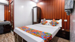 A hotel room with a bed, wooden panel walls, a mirror, and a nightstand. - Via Garden Inn (Mumbai)