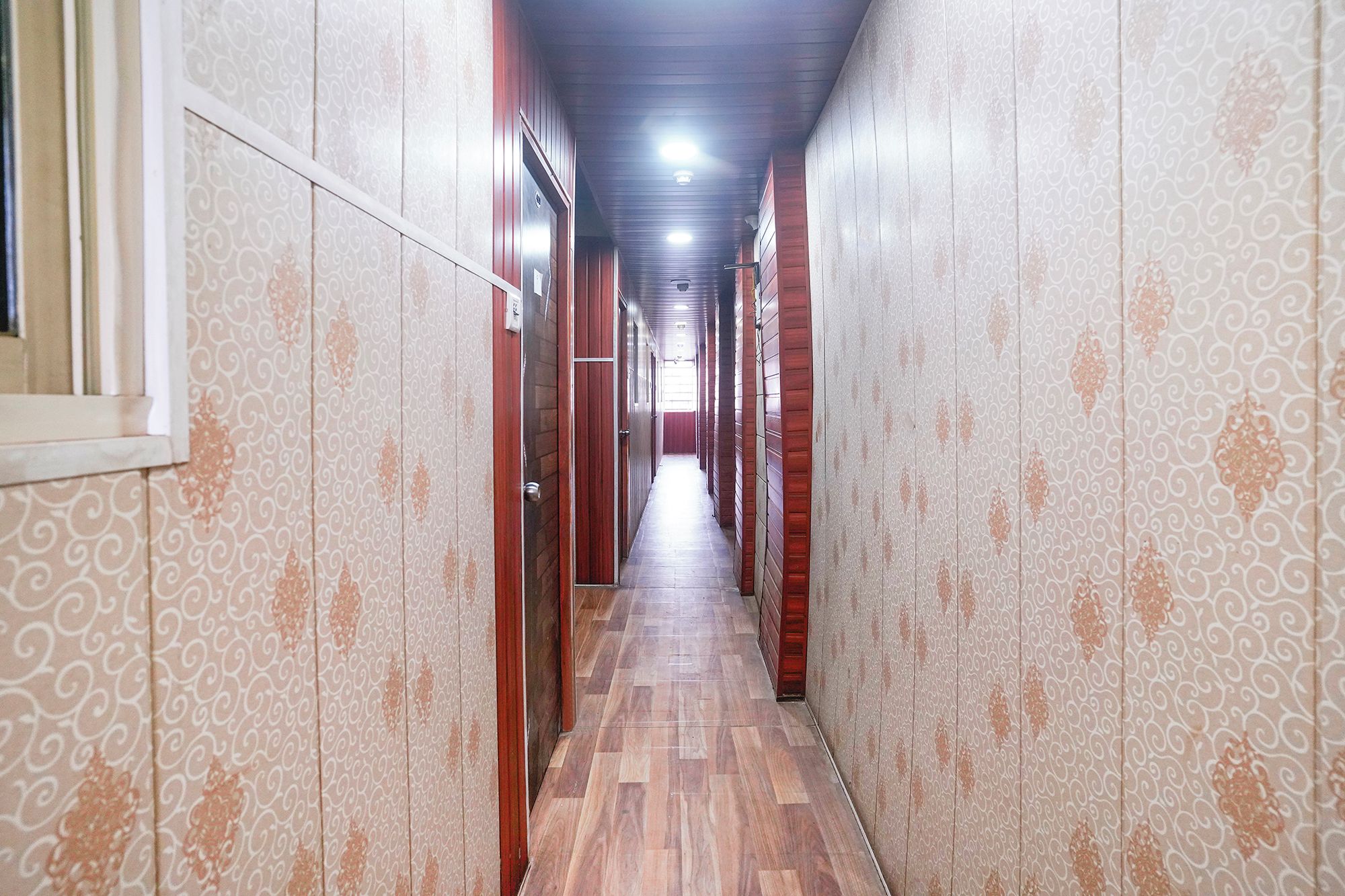 Un couloir aux murs ornés de motifs et au plancher en bois, qui mène à une porte au fond.