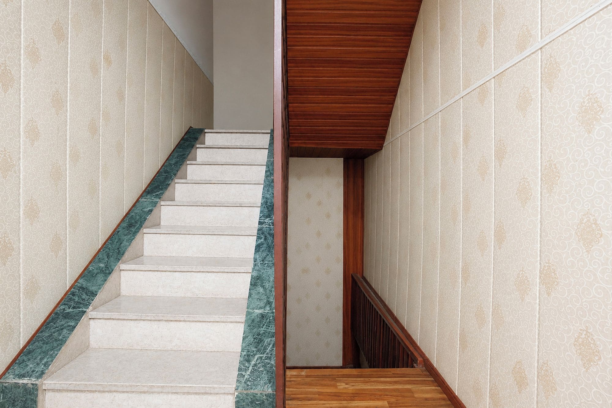 A staircase with a marble handrail and wooden steps, leading to a room with patterned wallpaper.