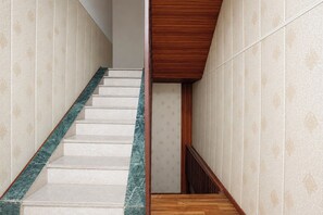 A staircase with a marble handrail and wooden steps, leading to a room with patterned wallpaper.