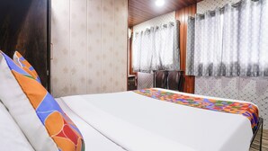 A hotel room with a bed, a window with curtains, a wooden ceiling, and a patterned wall. - Via Garden Inn (Mumbai)