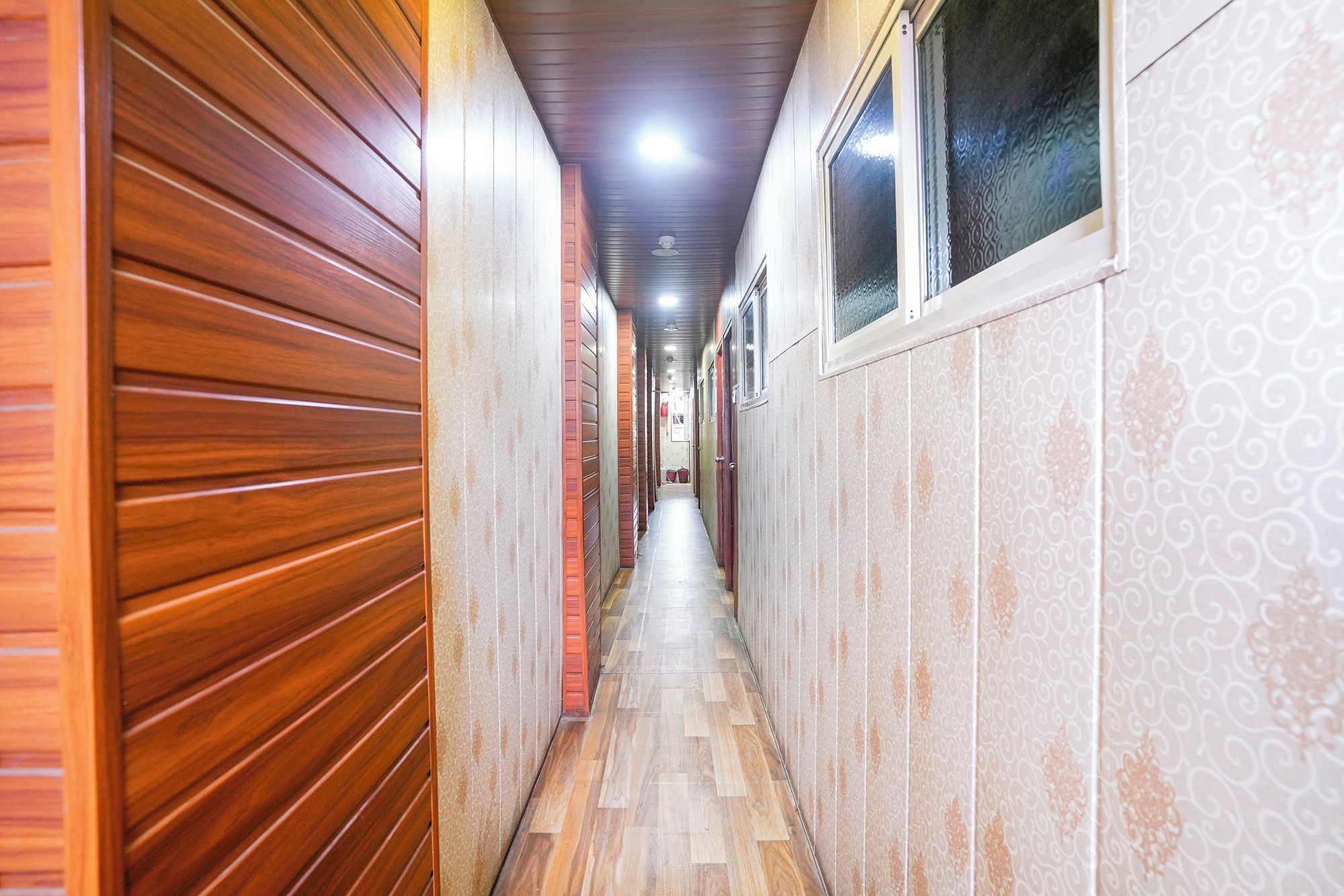A narrow hallway with wooden paneling on one side and patterned wallpaper on the other, leading to a door at the end.