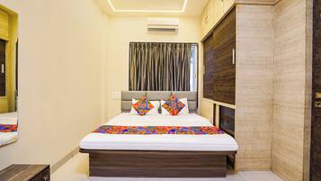 A bedroom with a bed, a headboard, a window with curtains, an air conditioning unit, and a wooden wardrobe.