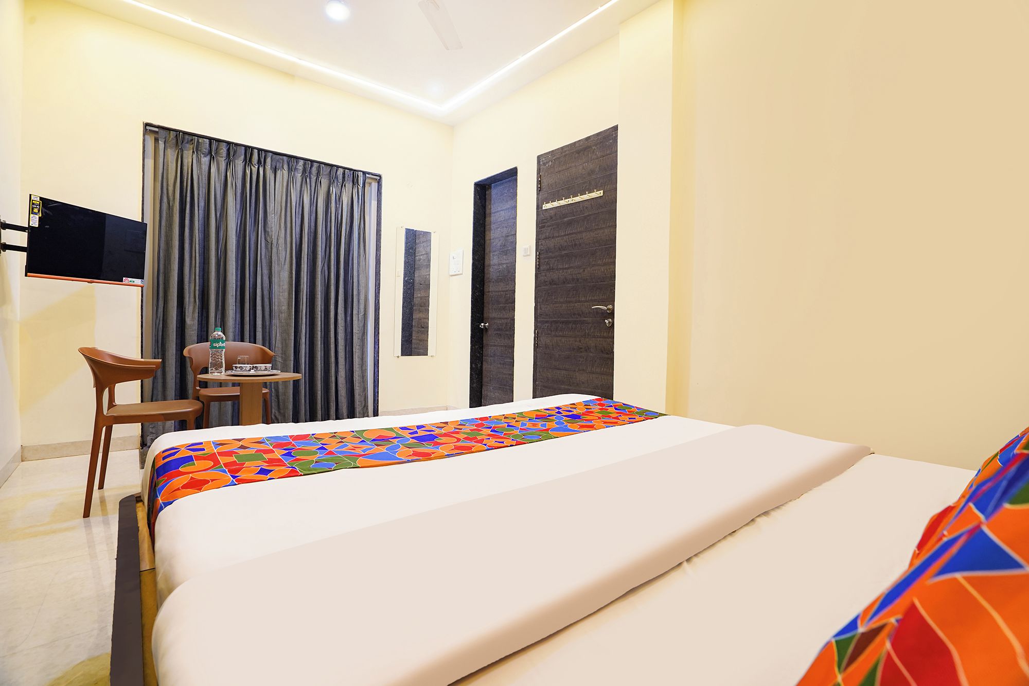 A hotel room with a bed, a desk with a chair, a television, and a window with curtains.