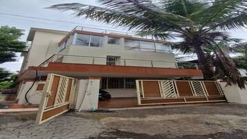 Un edificio de dos pisos con entrada protegida por un portón, un balcón visible y una palmera en primer plano.