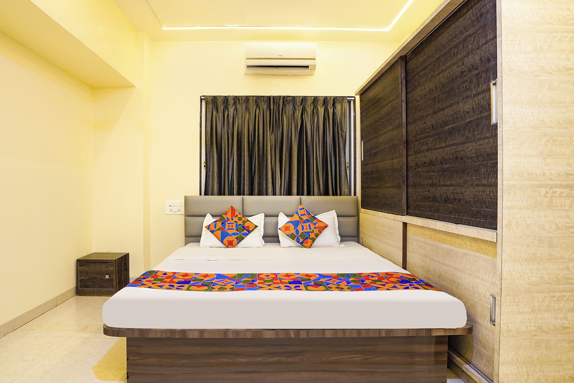 A bedroom with a bed, a bedside table, a wardrobe, and a curtain.