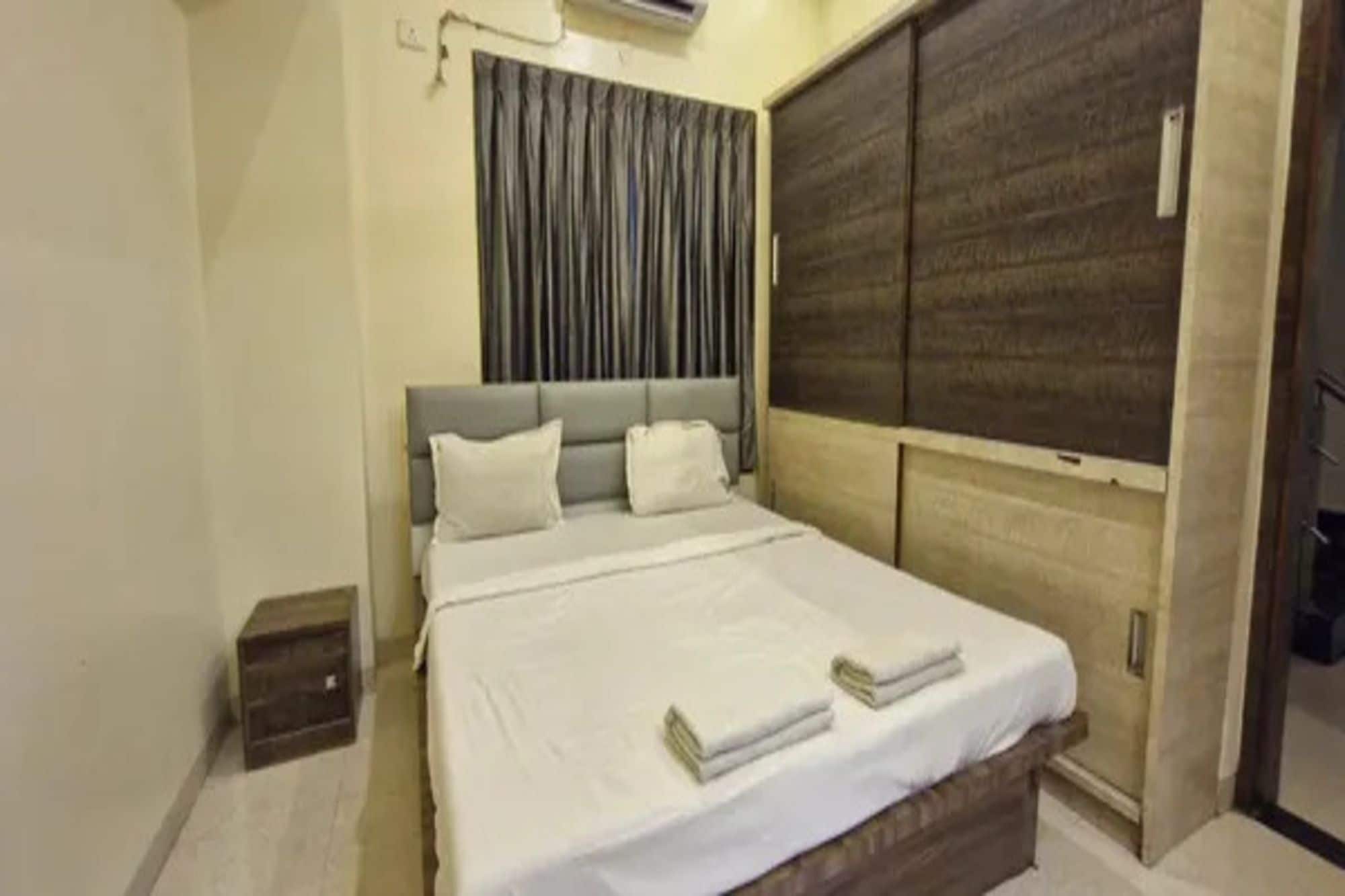 Un dormitorio con cama, mesita de noche, armario y ventana con cortinas.