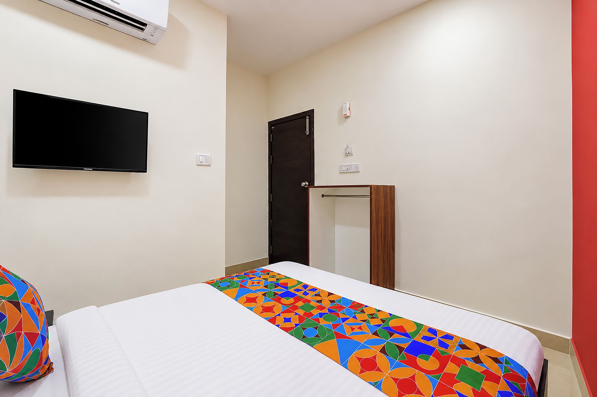 A hotel room with a bed, a flat-screen TV mounted on the wall, a door, and a small table.