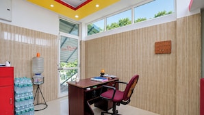 Una habitación con escritorio, silla, dispensador de agua y vistas por la ventana.