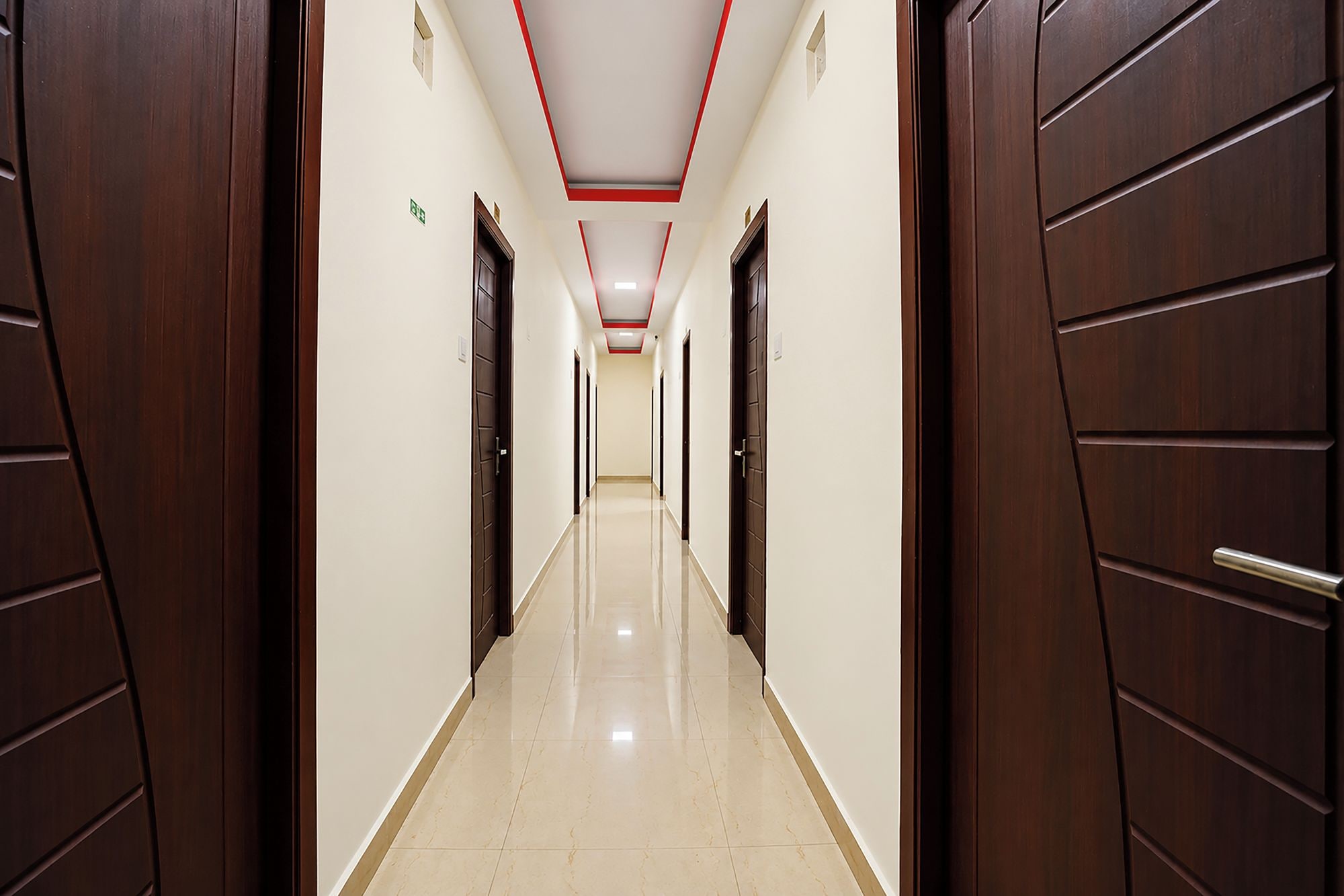 Un couloir avec des portes de chaque côté, un sol carrelé et un plafond orné de moulures rouges.