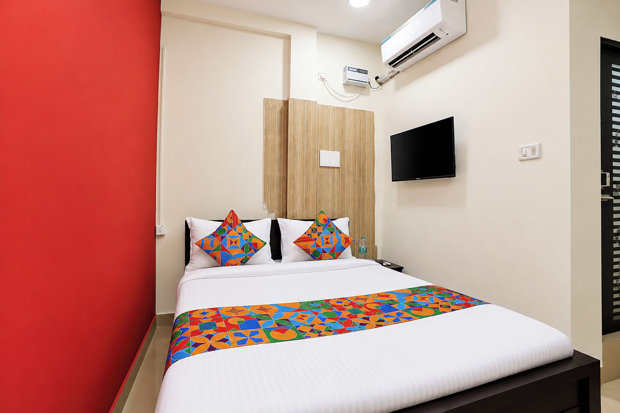 Ein Hotelzimmer mit Bett, einem an der Wand montierten Fernseher, einer Klimaanlage und einer roten Akzentwand.