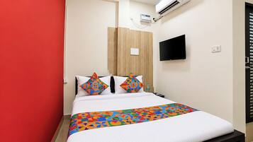 Ein Hotelzimmer mit Bett, einem an der Wand montierten Fernseher, einer Klimaanlage und einer roten Akzentwand.