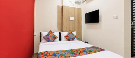 A hotel room with a bed, a wall-mounted TV, an air conditioning unit, and a red accent wall.