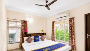 Habitación de hotel con cama, ventilador de techo, aire acondicionado y cortinas.