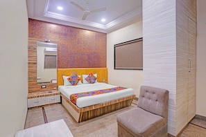 A hotel room with a bed, a chair, a wardrobe, a mirror, and a ceiling fan. - Fabhotel Chaya (Chhatrapati Sambhajinagar)