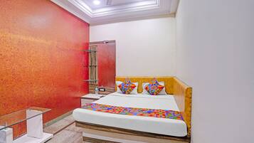 Habitación de hotel con cama, mesita de noche, espejo y una pared de acento roja.
