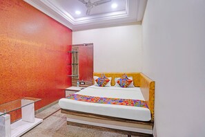 A hotel room with a bed, a nightstand, a mirror, and a red accent wall.