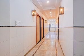 A hotel hallway with white tiled walls, a polished floor, and wall-mounted lighting fixtures. - Fabhotel Chaya (Chhatrapati Sambhajinagar)
