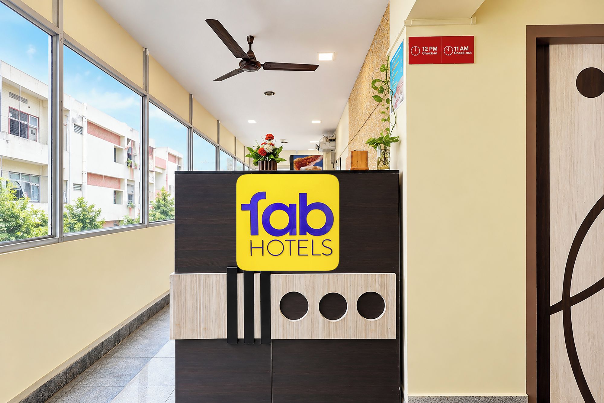 Ein Hotelrezeptionstresen mit einem Schild für 'fab hotels', einem Deckenventilator und einem Schild für Check-in/Check-out.