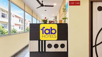 Ein Hotelrezeptionstresen mit einem Schild für 'fab hotels', einem Deckenventilator und einem Schild für Check-in/Check-out.