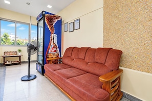Una habitación con sofá, ventilador, refrigerador Thums Up y ventana con vista.