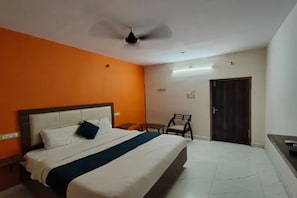 A hotel room with a bed, a chair, a desk, and a door. - Fabhotel Happy Grand (Vijayawada)