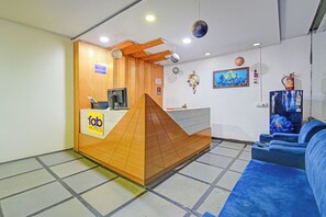 A hotel reception area with a wooden counter, a computer, and a blue sofa. - FabHotel Living Tree Suites (Hyderabad)