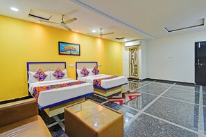 A hotel room with two beds, a glass coffee table, a painting on the wall, and a door with a decorative design. - FabHotel Living Tree Suites (Hyderabad)