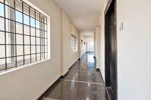 A corridor with a tiled floor, barred windows, and a door on the right. - FabHotel Living Tree Suites (Hyderabad)