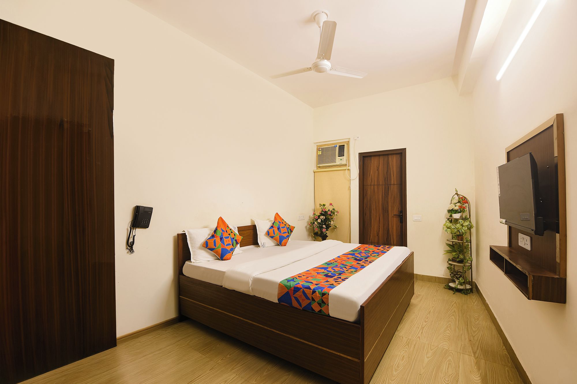 A bedroom with a bed, a ceiling fan, a TV, and a plant.
