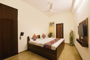 A bedroom with a bed, a ceiling fan, a TV, and a plant. - FabHotel Cozi Inn (Gurugram)