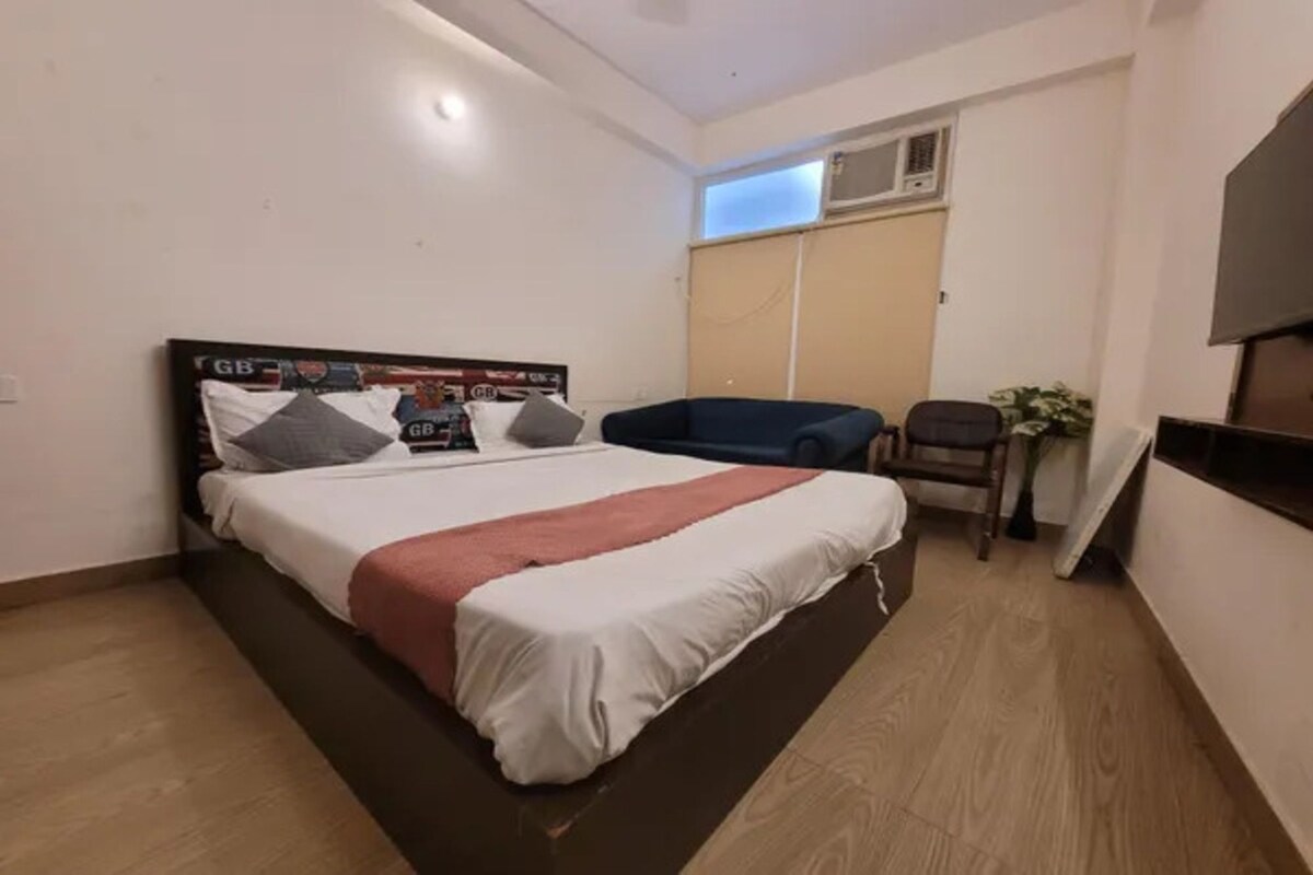A bedroom with a bed, a chair, a small table, and a potted plant.