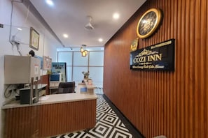 A reception area with a wooden reception desk, a clock, and a sign for 'Cozzi Inn.' - Fabhotel Cozi Inn (Gurugram)