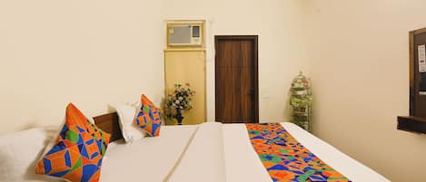 A hotel room with a bed, pillows, a door, a wall-mounted air conditioner, and a small plant.
