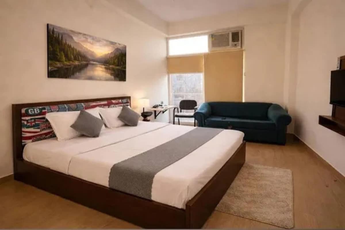 A hotel room with a bed, a desk, a chair, a sofa, and a TV.