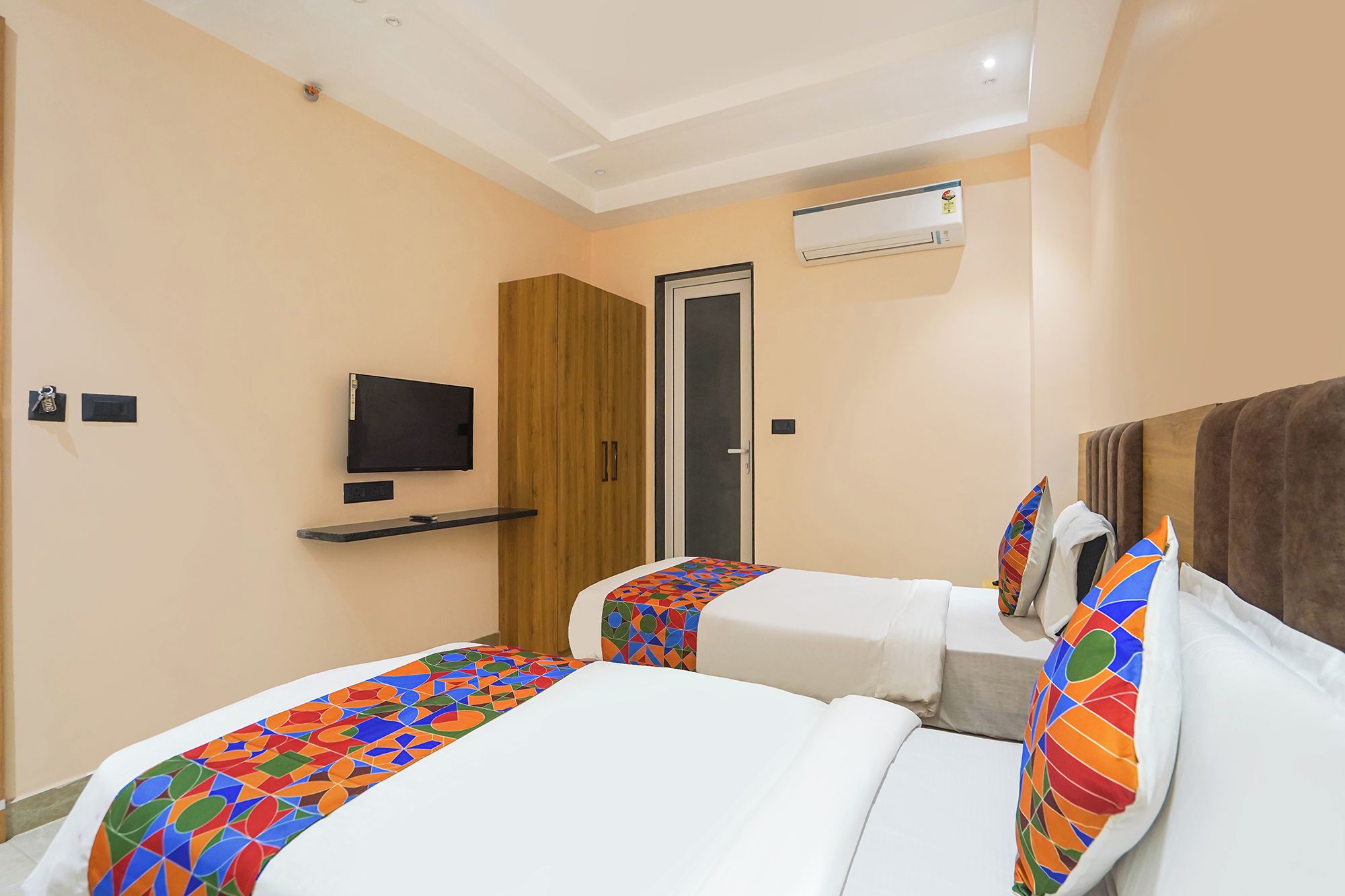 A hotel room with two beds, a TV, and an air conditioning unit.