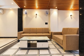 A modern living room with a sofa, a coffee table, and wall-mounted fans. - FabHotel Shri Hari Villa (Varanasi)