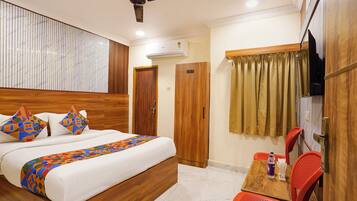 A hotel room with a bed, a wooden headboard, a ceiling fan, a TV, a window with curtains, and a small table with a bottle and chopsticks.