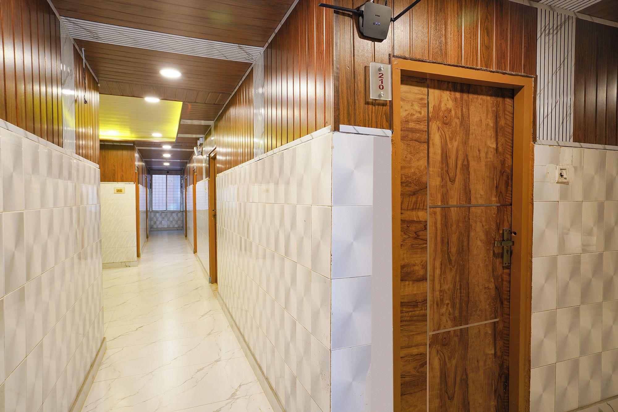 A hallway with wooden paneling and white tiled walls, leading to a door with a number plate.