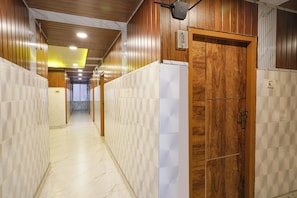 A hallway with wooden paneling and white tiled walls, leading to a door with a number plate. - FabHotel Sry Grand (Hyderabad)