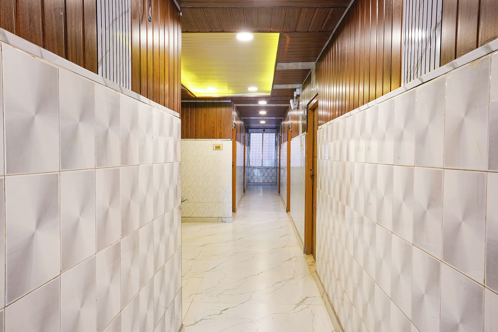 A corridor with tiled walls and a marble floor, leading to a door with a window at the end.