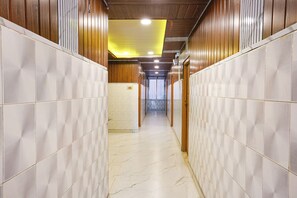 Un couloir aux murs recouverts de carreaux et au sol en marbre, qui mène à une porte avec une fenêtre au bout.