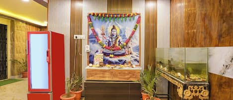 A room with a mural of a deity, a red refrigerator, potted plants, and a fish tank.