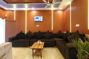 Un salon moderne avec un canapé d’angle, une table basse en bois et un téléviseur fixé au mur.