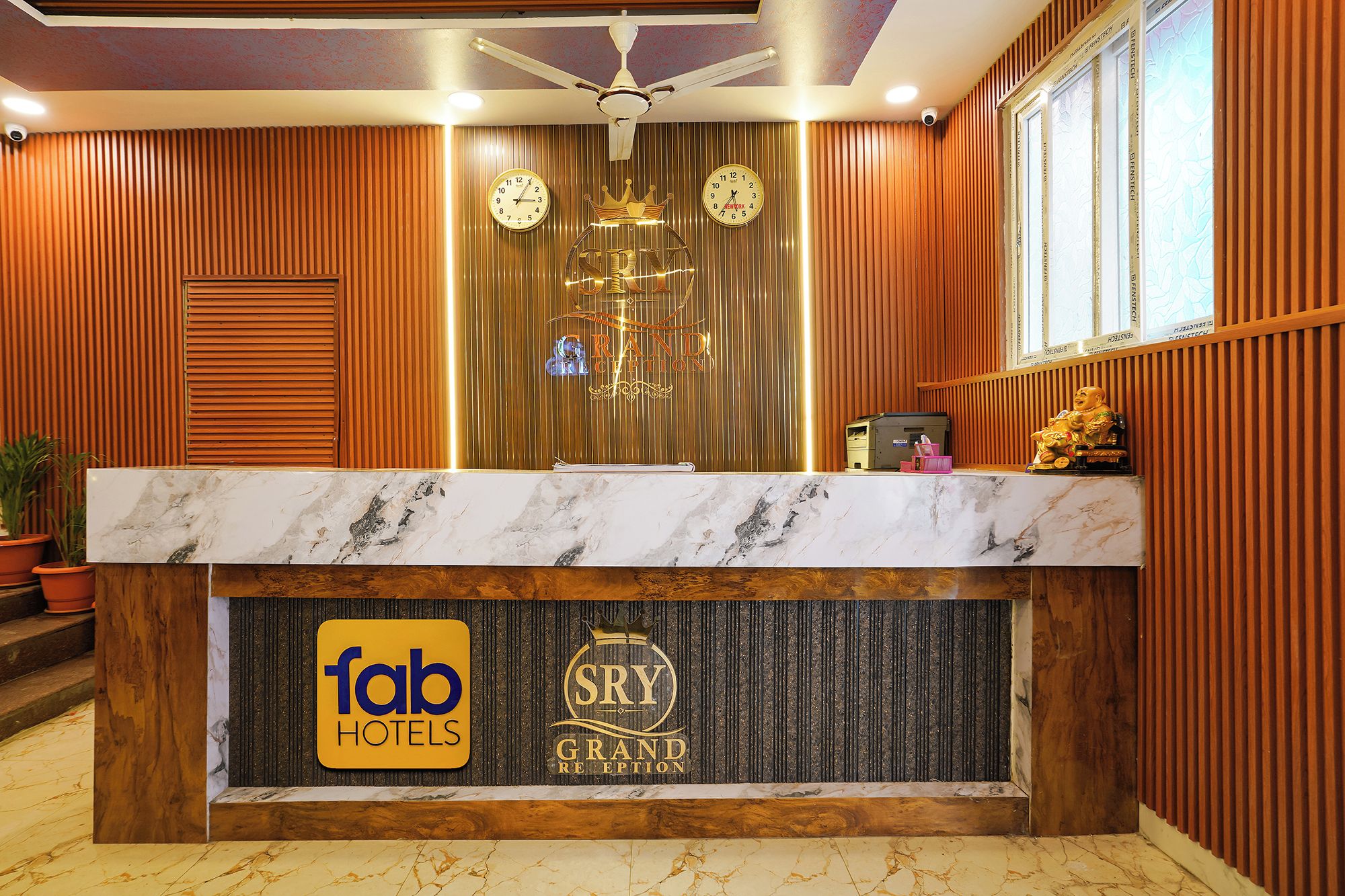A hotel reception desk with a marble top, wooden paneling, and a ceiling fan.